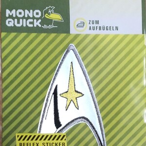 Könnte beinhalten: Ein weiß-grauer Bügelaufkleber mit einem gelben Stern in der Mitte. Der Aufkleber hat die Form eines spitzen Dreiecks mit abgerundeten Kanten. Der Text "REFLEX STICKER" ist in Gelb auf einem schwarz-gelb gestreiften Hintergrund gedruckt. Der Text "HOCHREFLEX MATERIAL DIN 3071 SICHERHEIT BEI NACHT!" ist in Schwarz auf gelbem Hintergrund gedruckt.