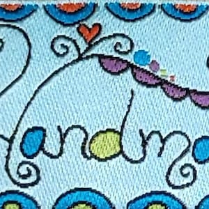 Può includere: Un'etichetta in tessuto blu con un disegno a mano di un cuore, vortici e la parola "Handmade".