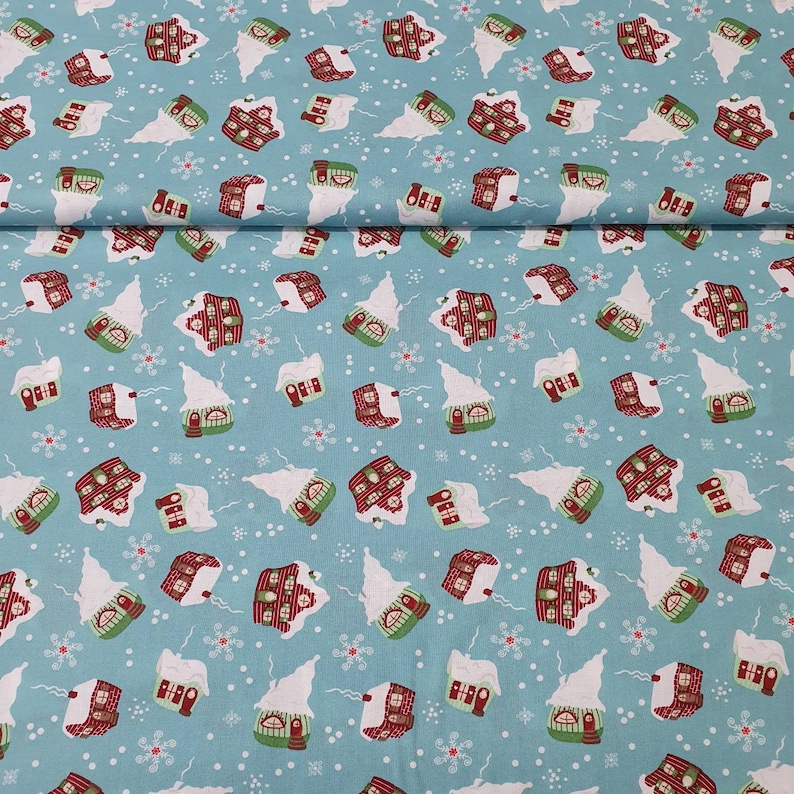 May include: Light blue fabric with a repeating pattern of snow-covered houses and snowflakes. The houses have red roofs, green doors, and white snow. A festive, winter-themed fabric.