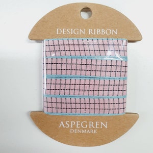 Könnte beinhalten: Eine Spule mit rosa-blauem gemustertem Band mit schwarzen Punkten. Das Band ist auf einer braunen Pappspule verpackt, auf der "DESIGN RIBBON" und "ASPEGREN DENMARK" aufgedruckt sind.