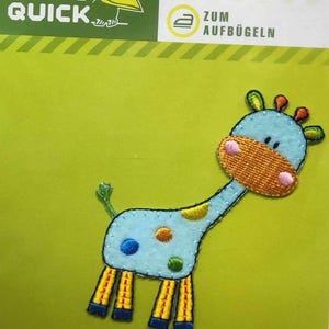 Könnte beinhalten: Ein blaues und gelbes Bügelbild mit einer Cartoon-Giraffe mit orangefarbenen Flecken. Das Bügelbild sagt "Zum Aufbügeln", was "Zum Aufbügeln" auf Deutsch bedeutet.