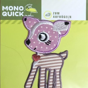 Pode incluir: Um remendo de ferro com um veado de desenho animado com listras rosa e marrom, bolinhas brancas e um coração vermelho. O remendo diz "Zum Aufbügeln", que significa "Passar a ferro" em alemão.