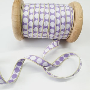 Op de afbeelding: Een spoel met lavendel lint met witte stippen en een gele rand. Het lint is om een houten spoel gewikkeld.