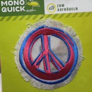 Könnte beinhalten: Ein weißes Peace-Zeichen mit blauer Umrandung und roter Mitte. Der Patch ist an den Rändern ausgefranst und hat auf der Verpackung den Schriftzug "Zum Aufbügeln".