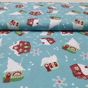 May include: Light blue fabric with a repeating pattern of snow-covered houses in red, green, and white. The houses have chimneys and are surrounded by snowflakes and white snow drifts. A festive, winter-themed textile.