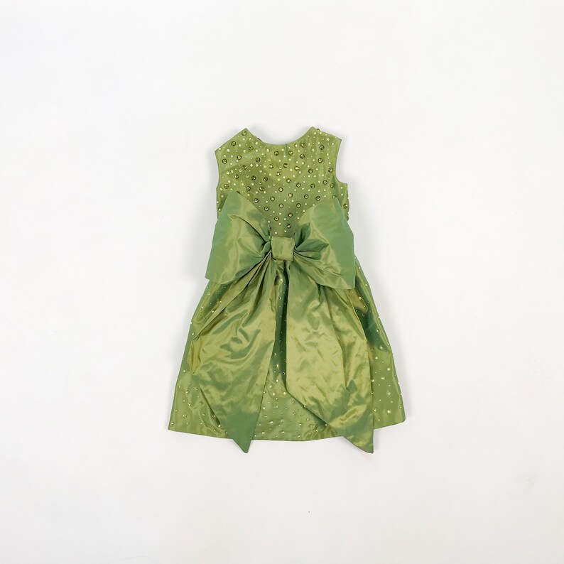 May include: A green sleeveless dress with a large bow at the waist and a beaded bodice.