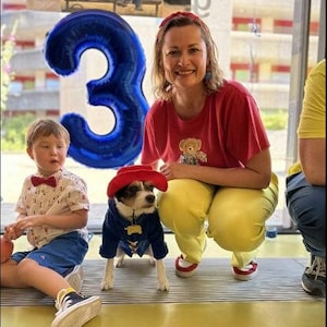 Miss Teddy customers model the Paddington Bear Outfit with a blue overcoat complete with white wooden toggles and a large oversized red hat just like Paddington.