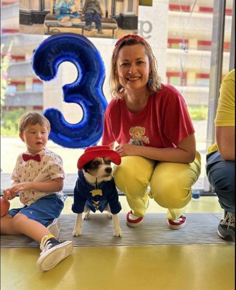 Miss Teddy customers model the Paddington Bear Outfit with a blue overcoat complete with white wooden toggles and a large oversized red hat just like Paddington.