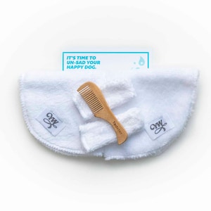 May include: A set of dog grooming tools including two white microfiber cloths, a wooden comb, and a card with the text "It's time to un-sad your happy dog."