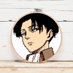 Op de afbeelding: Een zwart-witte pixel art borduurring met een portret van een jonge man met zwart haar en bruine ogen. Hij draagt een bruin jack en een wit shirt.