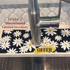 May include: A black and white daisy print sink protector, measuring 15" x 5 3/4", is positioned under a faucet. The text "Discontinued Limited Inventory" is visible. A "SPECIAL OFFER" sticker is also present.