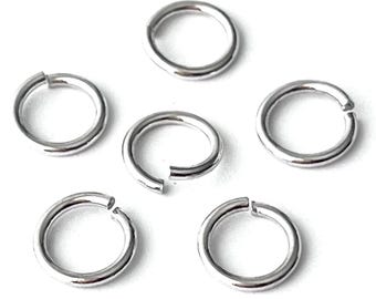 May include: A collection of silver-colored jump rings, some open and some closed, against a white background. These small, circular metal rings are commonly used in jewelry making and crafting projects.