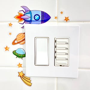 May include: A white light switch with a timer. The timer has six buttons labeled 10M, 20M, 30M, 60M. The switch is decorated with colorful space-themed stickers, including a rocket, a planet, a UFO, and stars.