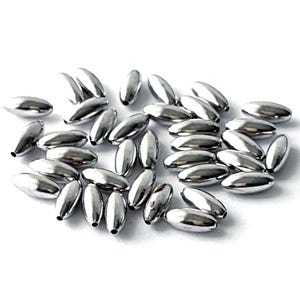May include: A collection of shiny, silver-colored fishing weights, each with a teardrop shape. The weights are scattered on a white surface, reflecting light and creating highlights. These weights are designed for angling.