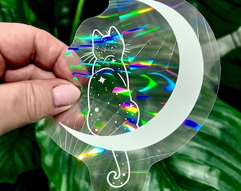 May include: A holographic sticker featuring a white outline of a cat sitting on a crescent moon. The cat is covered in small white stars.
