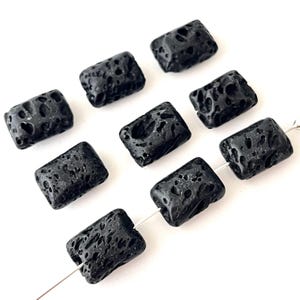 May include: A collection of rectangular black lava rock beads with a porous texture. The beads are strung on a thin, silver-colored wire, and are displayed against a white background. These beads are suitable for jewelry making.