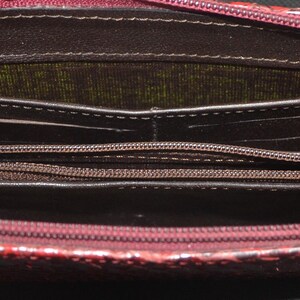 May include: Open burgundy wallet with multiple compartments and a zippered coin pocket. The wallet has a textured exterior and a dark interior with visible stitching. The zipper is silver-toned.