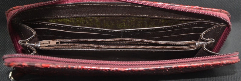 May include: Open burgundy wallet with multiple compartments and a zippered coin pocket. The wallet has a textured exterior and a dark interior with visible stitching. The zipper is silver-toned.