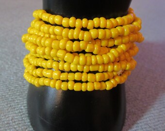 May include: A stack of yellow beaded bracelets. The bracelets are made of small, round beads that are strung together to form a continuous loop.