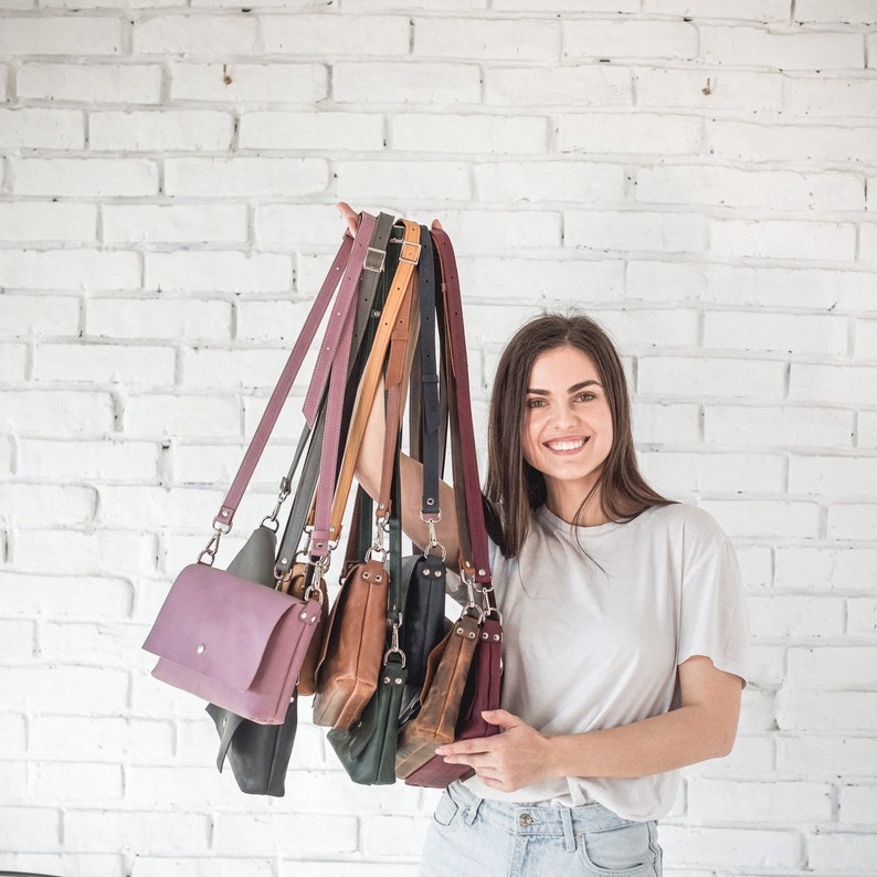 Pu&ograve; includere: Una donna tiene in mano una pila di sette borse a tracolla in pelle di diversi colori. Le borse sono di diverse dimensioni e stili, e sono tutte realizzate in pelle di alta qualit&agrave;.