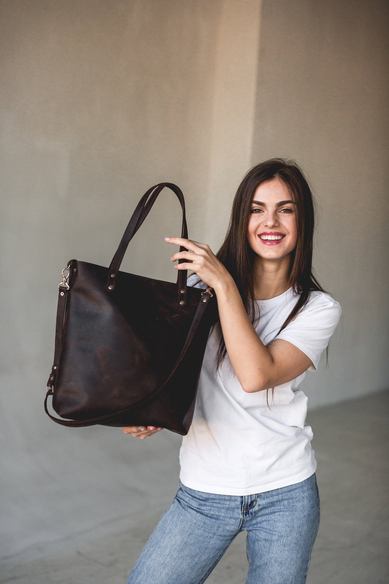 Woman holding large handmade dark brown leather tote bag with shoulder and crossbody strap