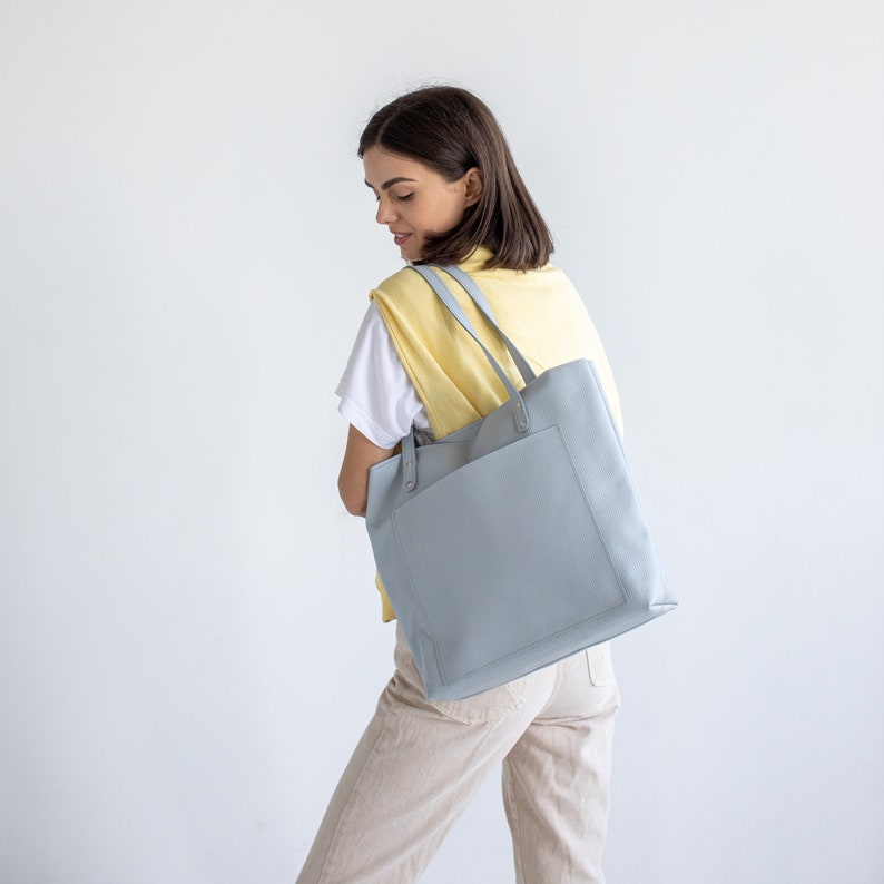 May include: A light blue tote bag with a yellow top and a white shirt underneath. The bag has a single pocket on the front.