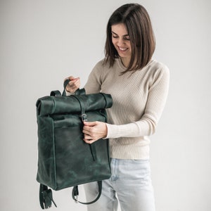 May include: A dark green leather roll top backpack with a silver buckle.