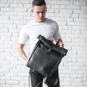 May include: A black leather backpack with a roll-top closure and a buckle strap.