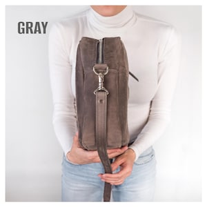 Pode incluir: Bolsa de ombro cinza de camur&ccedil;a com z&iacute;per e ferragens prateados. A bolsa tem uma al&ccedil;a longa e ajust&aacute;vel. A palavra "GRAY" est&aacute; impressa em letras grandes e em negrito no canto superior esquerdo da imagem.