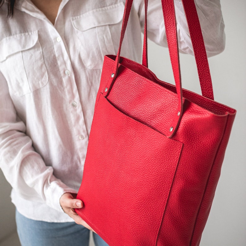 May include: A bright red leather tote bag with a front pocket. The bag has a top handle and two shoulder straps.