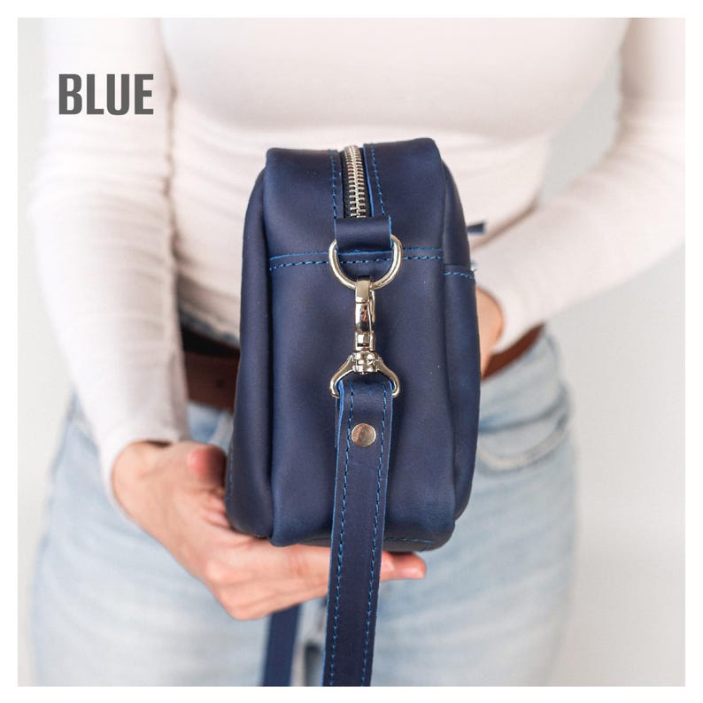Pode incluir: Uma bolsa transversal de couro azul marinho com z&iacute;per e ferragens prateadas. A bolsa tem uma al&ccedil;a longa e ajust&aacute;vel. A palavra "BLUE" est&aacute; impressa no canto superior esquerdo.