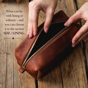 May include: A brown leather rectangular pouch with a gold zipper is open, revealing a black interior. The text "What can be with lining or without - and you can choose it in the section SIZE / LINING" is visible. The pouch is on a wooden surface.