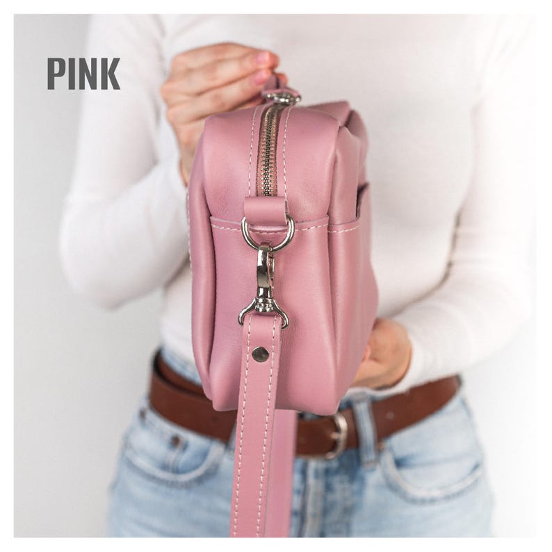 Pode incluir: Uma bolsa transversal de couro rosa com z&iacute;per e ferragens de al&ccedil;a prateadas. A bolsa tem formato retangular e uma al&ccedil;a remov&iacute;vel. A palavra "PINK" est&aacute; impressa no canto superior esquerdo.