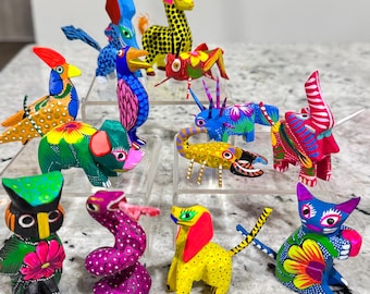 Pode incluir: Uma coleção de 13 figuras de animais de madeira pintadas à mão. As figuras são coloridas e apresentam uma variedade de animais, incluindo uma girafa, um galo, uma cobra, um gato, um cão, uma coruja, um pássaro, um elefante, um rinoceronte, um gafanhoto e um escorpião.