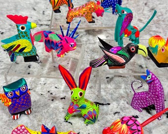 Pode incluir: Uma coleção de figuras de animais de madeira pintadas à mão e coloridas. As figuras são todas de animais diferentes, incluindo um galo, um tucano, um coelho, um gato, um morcego e um tatu. As figuras são todas de cores brilhantes e têm detalhes intrincados.