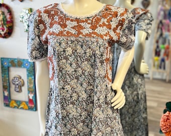 May include: A floral print dress on a mannequin. The dress features a brown bodice with white floral embroidery and a white lace trim. The skirt has a pattern of small flowers in shades of blue, white, and brown. The dress has short sleeves.
