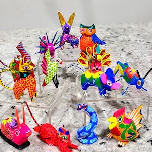 May include: A collection of 12 hand-painted wooden animal figurines. The figurines are brightly colored and feature a variety of animals, including a rabbit, owl, peacock, elephant, grasshopper, snake, cat, and rooster.