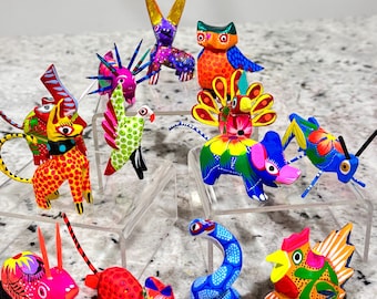 Pode incluir: Uma coleção de 12 figuras de animais de madeira pintadas à mão. As figuras são coloridas e apresentam uma variedade de animais, incluindo um coelho, uma coruja, um pavão, um elefante, um gafanhoto, uma cobra, um gato e um galo.