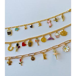 May include: Three gold chains with various charms, including a coffee cup, a heart, a skull, a cupcake, a mermaid tail, a sunflower, a ballerina, a daisy, a turtle, a rose, a star, a bee, a cat, a horseshoe, a letter P, a letter K, a cloud, a lotus flower, and a wing.