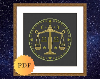 May include: A cross-stitch pattern featuring a golden Libra zodiac scale centered within a circular border on a dark gray background. The design includes small star and crescent moon motifs, with the text PDF displayed on a yellow starburst icon.