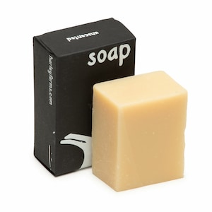 May include: A light beige, cube-shaped bar of soap next to a black box. The box has the word "soap" in white, stylized font, and the word "unscented" in smaller, white font. The website "harleyfarms.com" is also printed on the box.