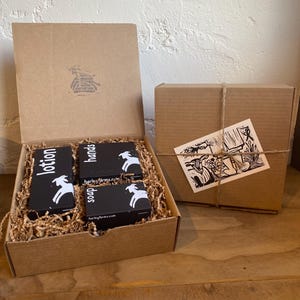 May include: A gift box set containing three small brown boxes with white goat illustrations and the text "harley farms.com" and "soap", "hands", and "lotion". The boxes are nestled in brown packing paper inside a larger brown box.