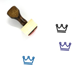 May include: A wooden stamp with a brown handle and a rectangular wooden block. The stamp features a black outline of a crown with three points. The stamp is on a white surface.