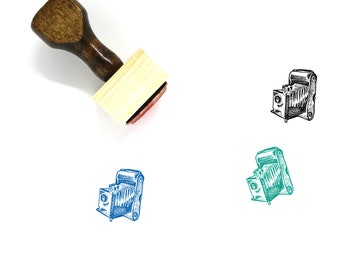May include: A wooden rubber stamp with a vintage camera design. The stamp is mounted on a wooden handle and has a red ink pad.