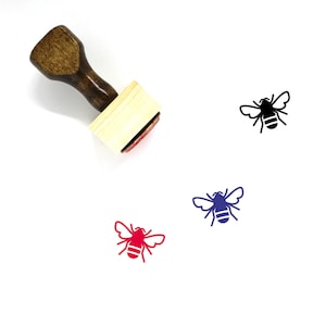 Puede incluir: Un sello de goma de madera con un diseño de abeja. El sello es rojo, negro y azul. El sello está sobre un fondo blanco.
