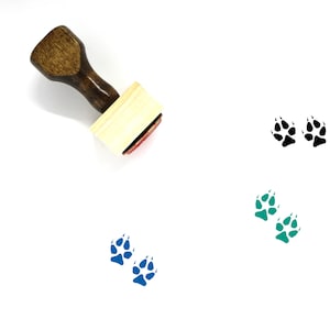 May include: A wooden stamp with a handle and a rectangular base. The stamp is designed to create paw prints. Three sets of paw prints are shown in black, blue, and green.