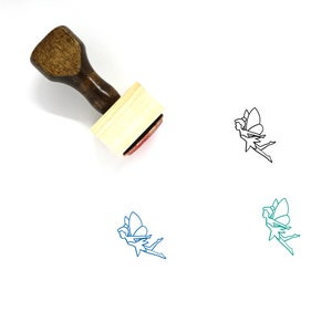 Puede incluir: Sello de madera con un diseño de hada. El sello es marrón con un mango de madera y una almohadilla de tinta roja. El hada está delineada en negro, azul y verde.