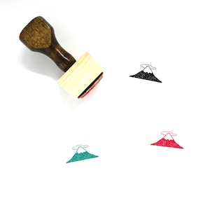 May include: A wooden stamp with a handle and a rectangular base. The stamp features a black and white illustration of a mountain with a cloud above it. The stamp is shown next to three other impressions of the mountain, one in black and white, one in green, and one in red.