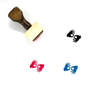 May include: A wooden rubber stamp with a handle and a rectangular base. The stamp features a black and white image of two hands forming the letter "O" in British Sign Language.