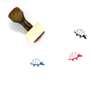 May include: A wooden rubber stamp with a brown handle and a rectangular base. The stamp features a black and white illustration of an armadillo. The stamp is on a white background.